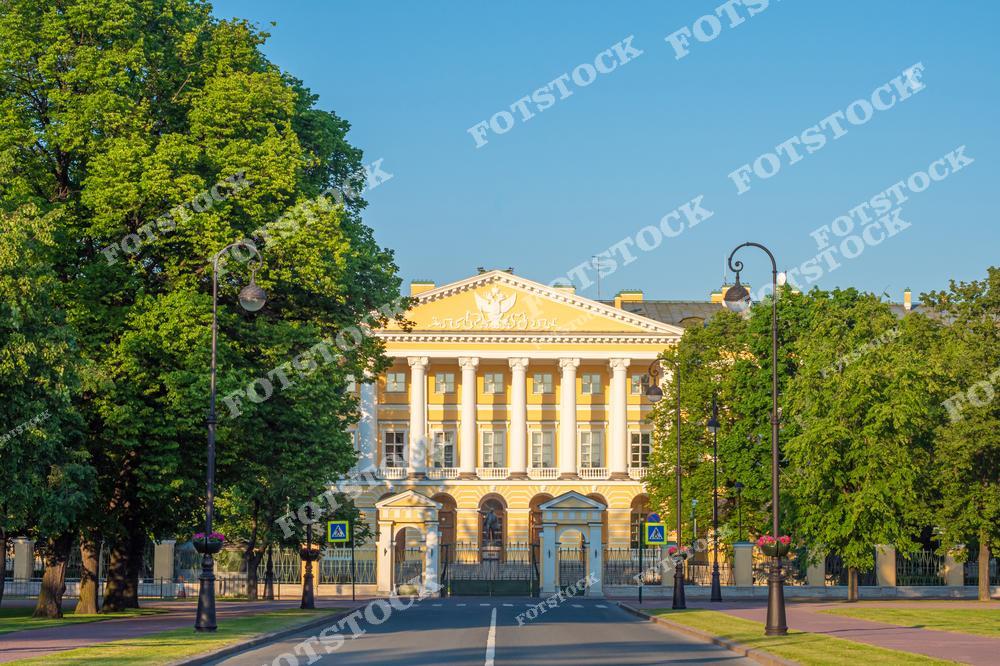 На фотографии изображено здание Смольного, расположенное в Санкт-Петербурге, исторически известное как Смольный институт благородных девиц, а позднее как центр политической деятельности. Классическое здание отличается строгими архитектурными формами, монументальными колоннами и гармоничными пропорциями. Вокруг здания зеленая территория, которая создает спокойный фон и подчеркивает его величие. Это здание является значимым памятником архитектуры и историческим символом города, а также резиденцией губернатора Санкт-Петербурга.